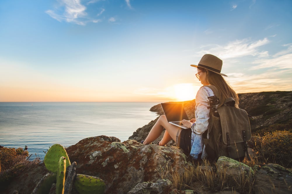 young female travel blogger sitting on the cliff top with laptop